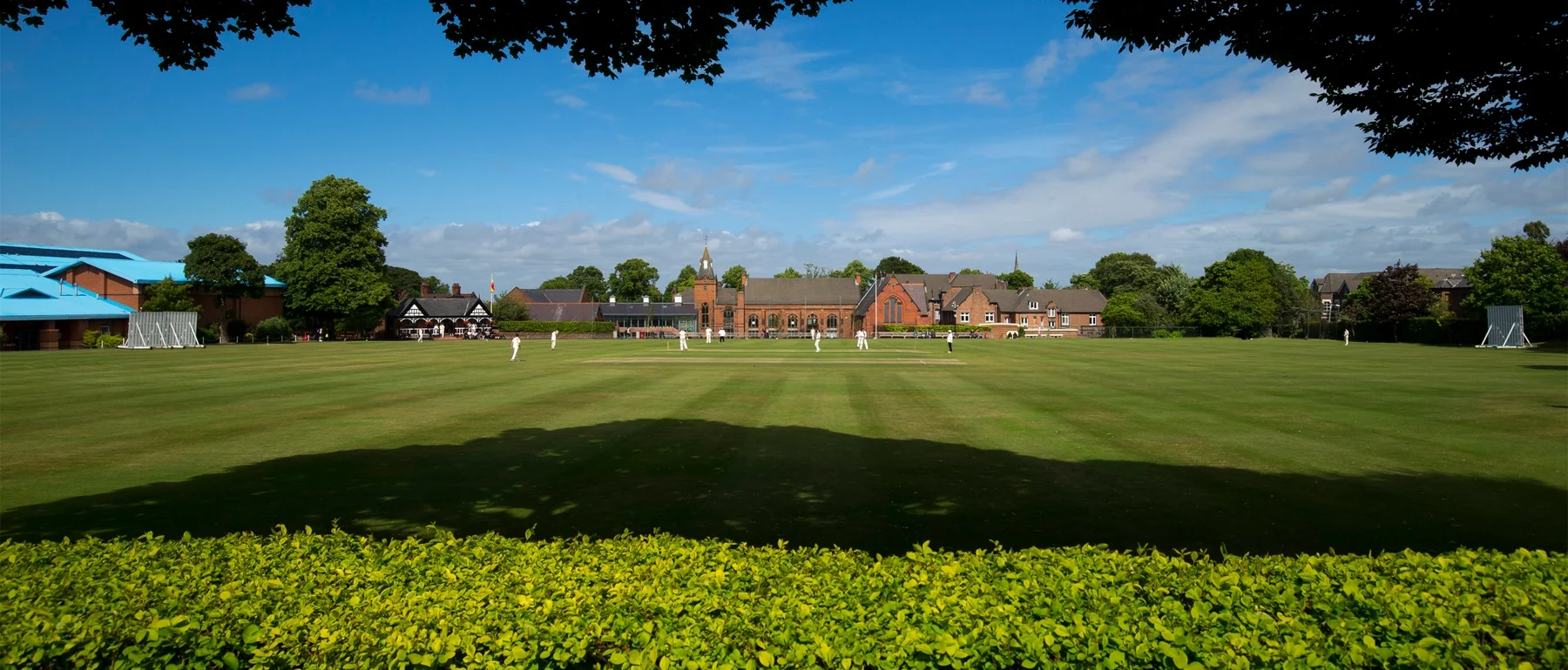 Birkenhead School cricket pitch shot through trees with the pavilion in the background